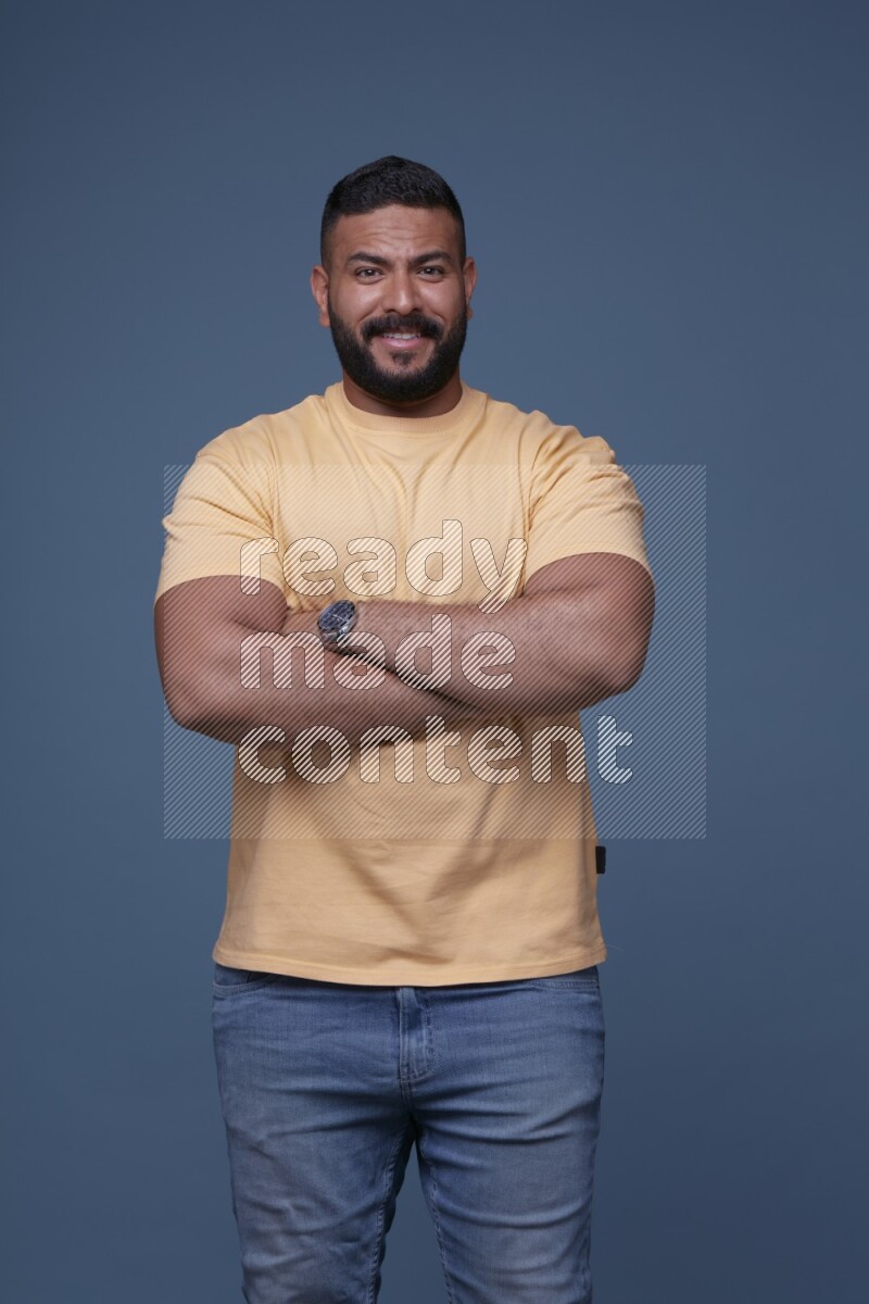 A man posing in a blue background wearing a yellow shirt