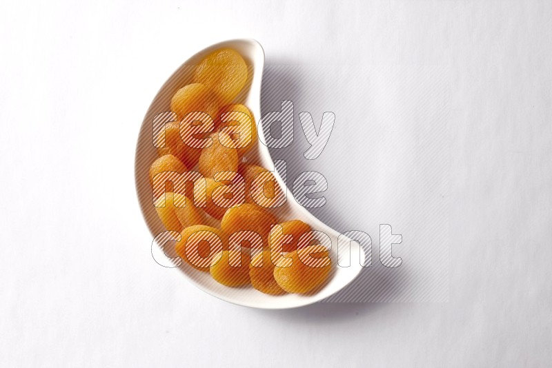Dried apricots in a crescent pottery plate on white background
