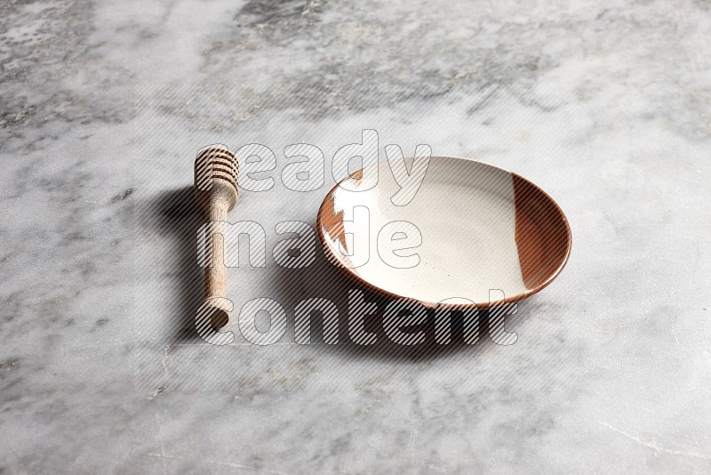 Multicolored Pottery Plate with wooden honey handle on the side with grey marble flooring, 45 degree angle