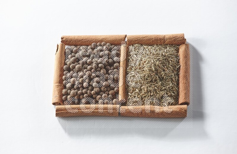 مربعان من أعواد القرفة ممتلئان ببهار الفلفل الحلو والكمون علي خلفية بيضاء