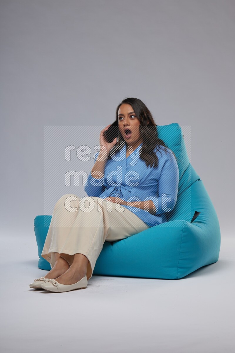 A woman sitting on a blue beanbag and talking on the phone