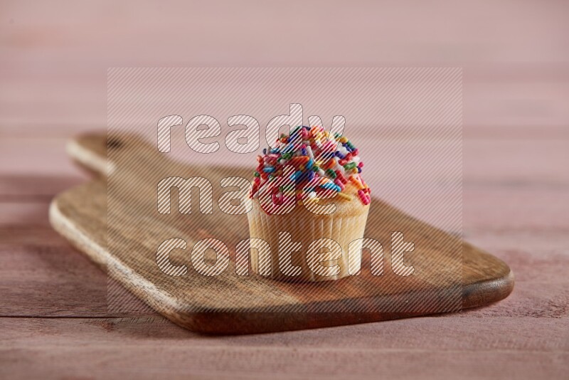 Vanilla mini cupcake topped with sprinkles on a wooden board