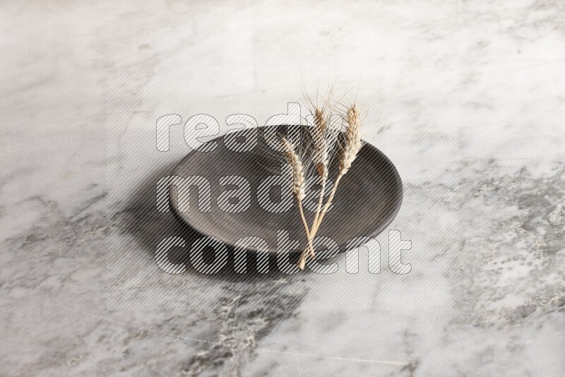 Wheat stalks on black pottery plate on grey marble background