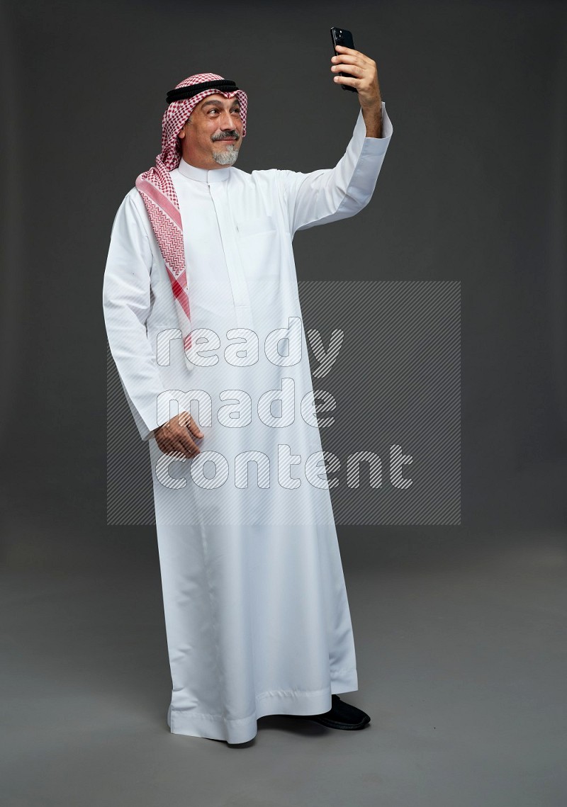 Saudi man with shomag Standing taking selfie on gray background