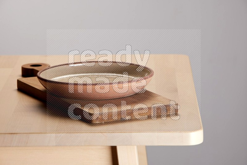 multi-colored pottery Plate placed on a  wooden rectangular cutting board on the edge of wooden table