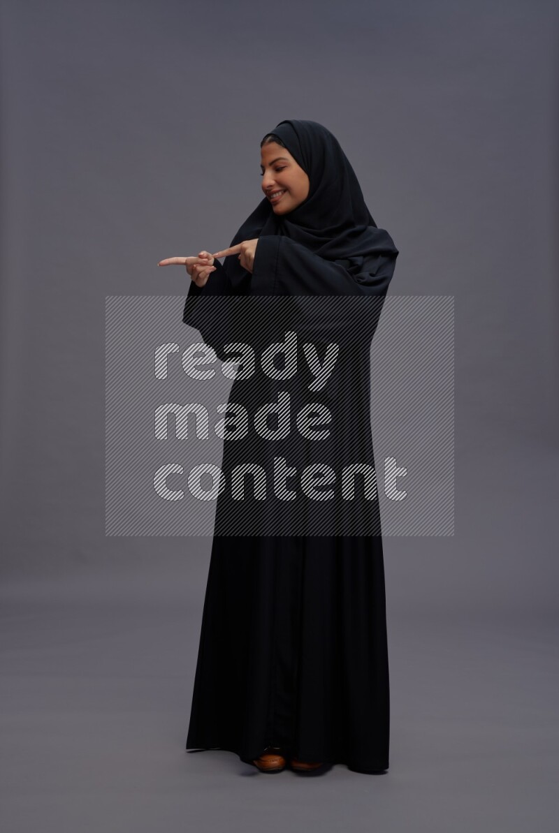 Saudi woman wearing Abaya standing interacting with the camera on gray background
