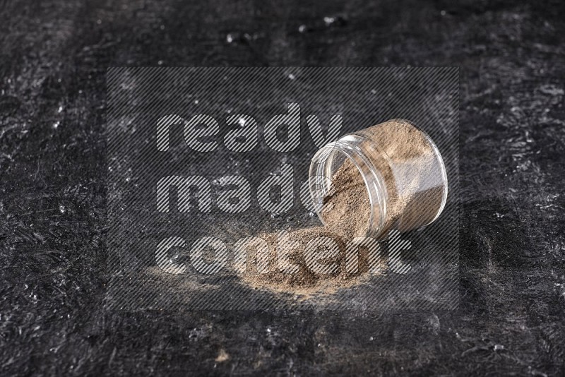 A flipped glass jar full of black pepper powder on a textured black flooring