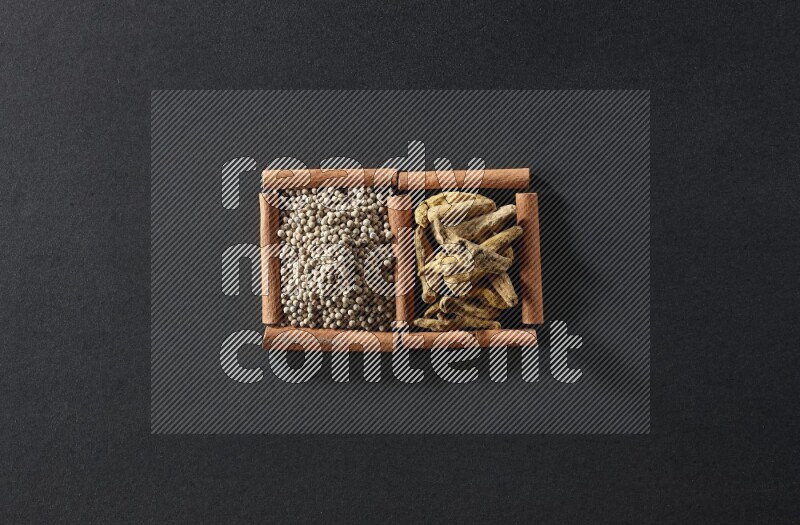 مربعان من أعواد القرفة ممتلئان بحبوب الفلفل الأبيض وأصابع الكركم علي خلفية سوداء