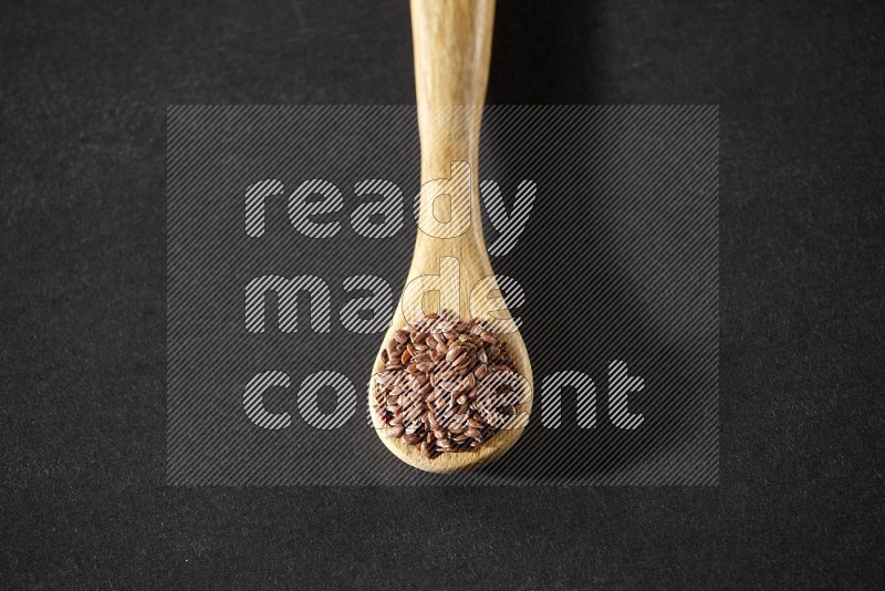 A wooden spoon full of flax on a black flooring in different angles