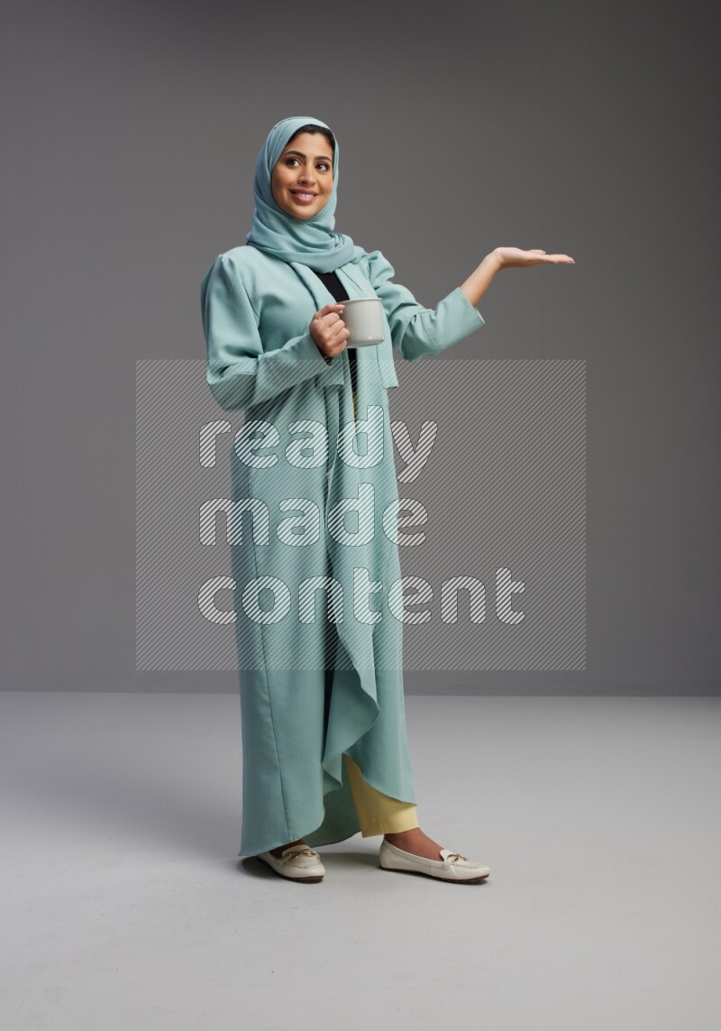 Saudi Woman wearing Abaya standing  holding a mug on Gray background