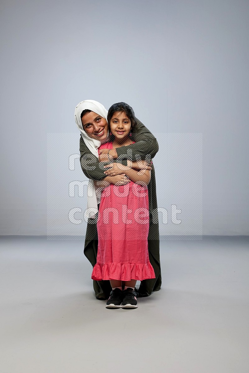 A girl and her mother interacting with the camera on gray background