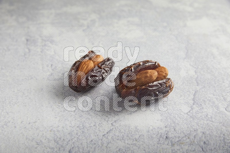 two almond stuffed madjoul dates on a light grey background