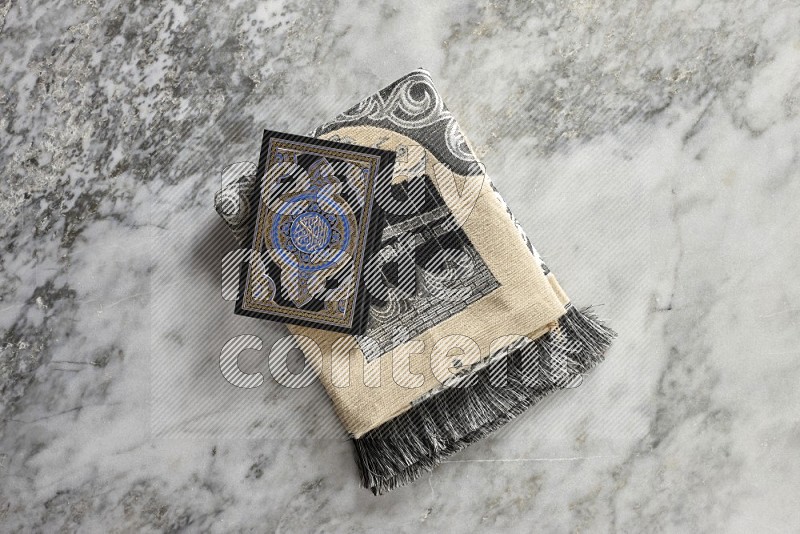 A prayer rug with different elements such as quran and prayer beads on grey marble background