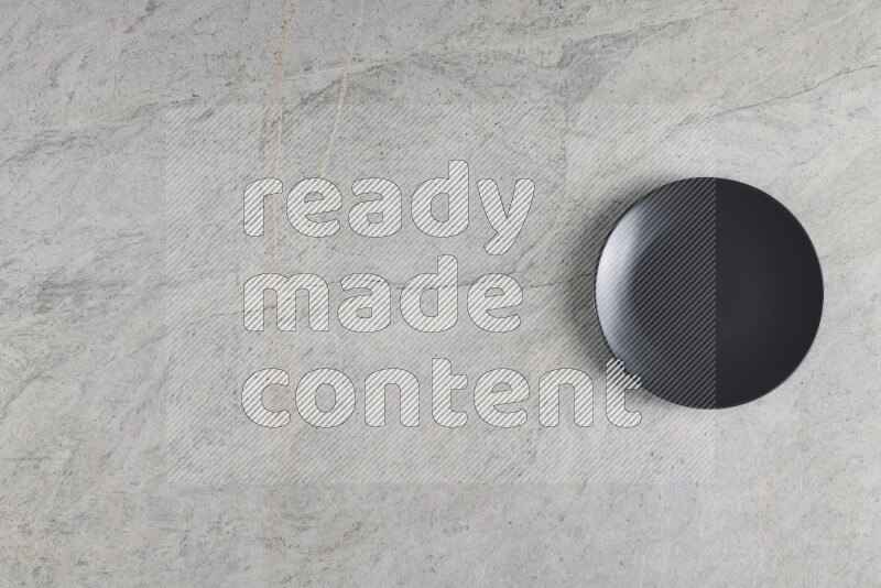A black ceramic circular plate on grey marble background