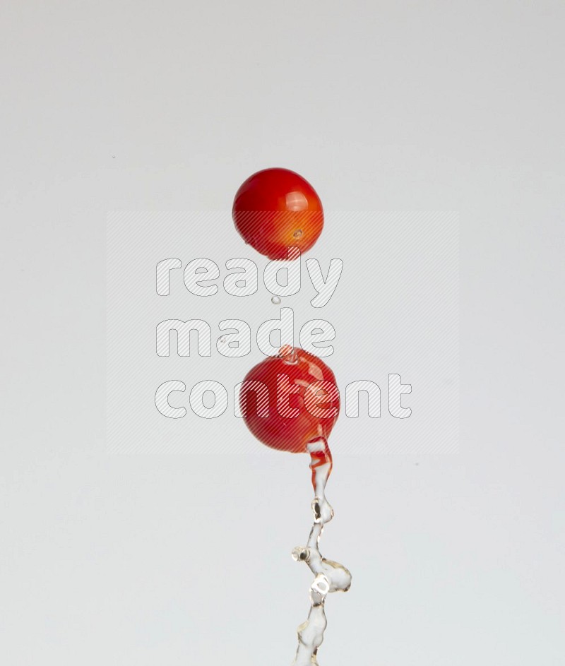 A metal spoon throwing two cherry tomatoes leaving a splash of water behind on a light blue background