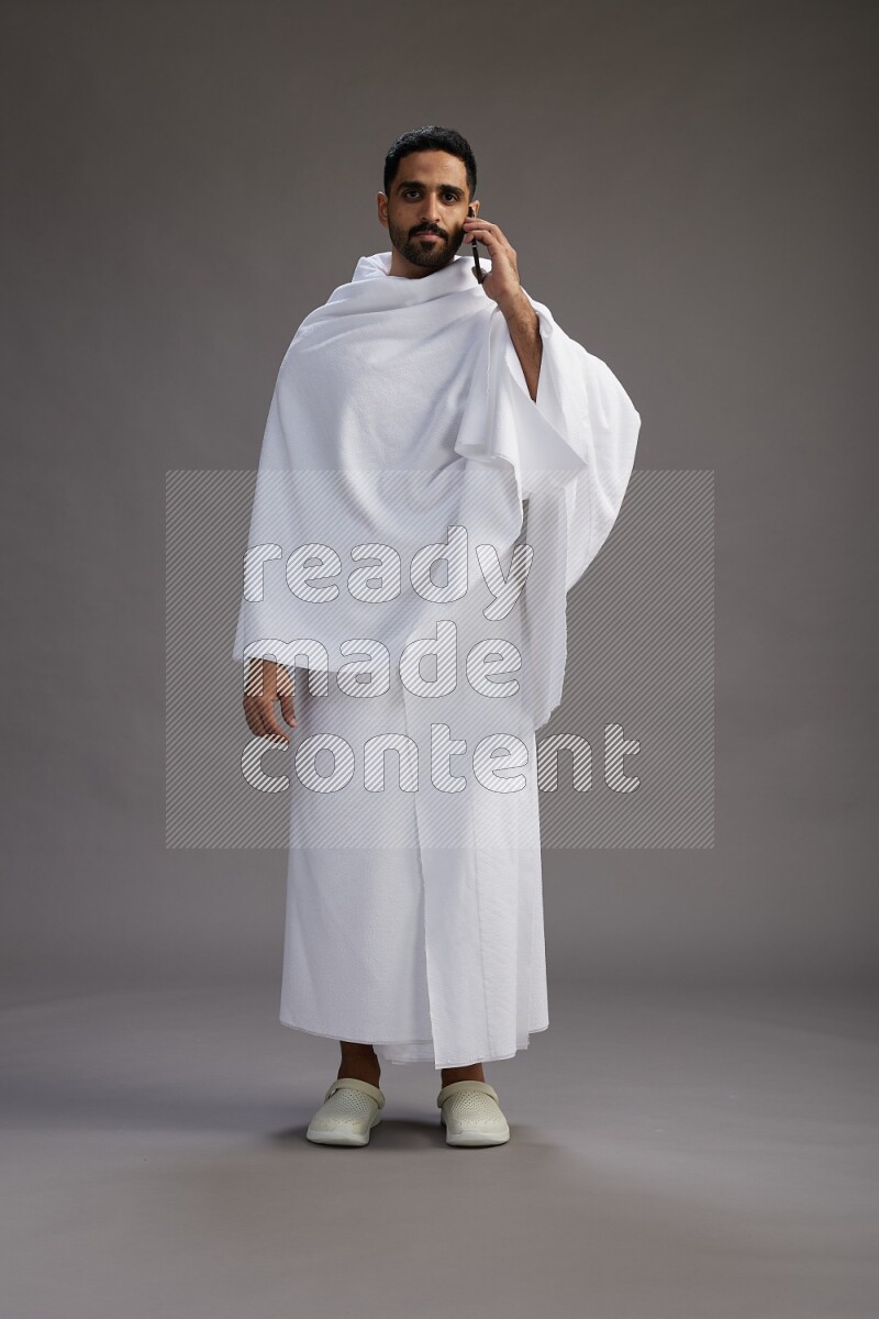 A man wearing Ehram Standing talking on phone on gray background