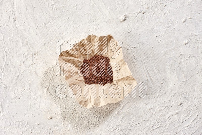 A crumpled piece of paper full of garden cress seeds on a textured white flooring