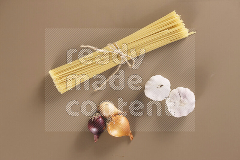 Raw pasta with different ingredients such as cherry tomatoes, garlic, onions, red chilis, black pepper, white pepper, bay laurel leaves, rosemary and cardamom on beige background