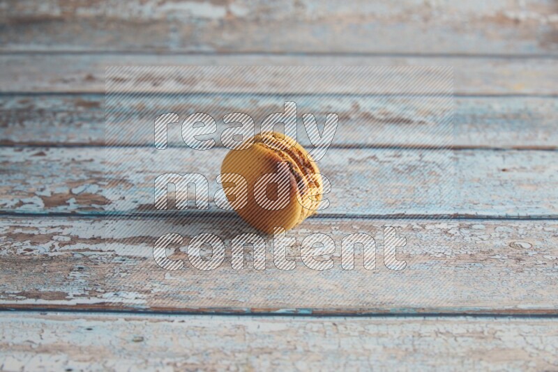 45º Shot of Yellow Crème Brulée macaron on light blue wooden background