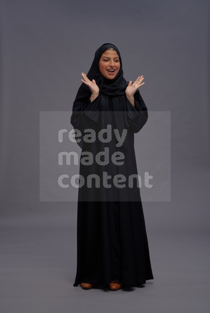 Saudi woman wearing Abaya standing interacting with the camera on gray background