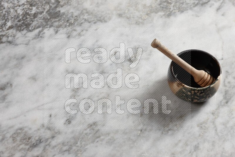 Multicolored pottery bowl with wooden honey dipper in it on grey marble background