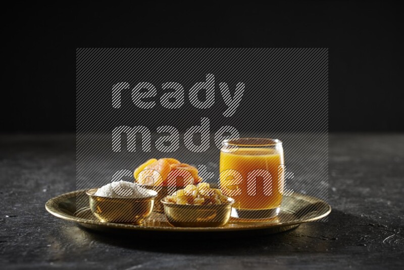 فواكه مجففة في أطباق معدنية مع مشروب قمر الدين على صينية علي خلفية سوداء