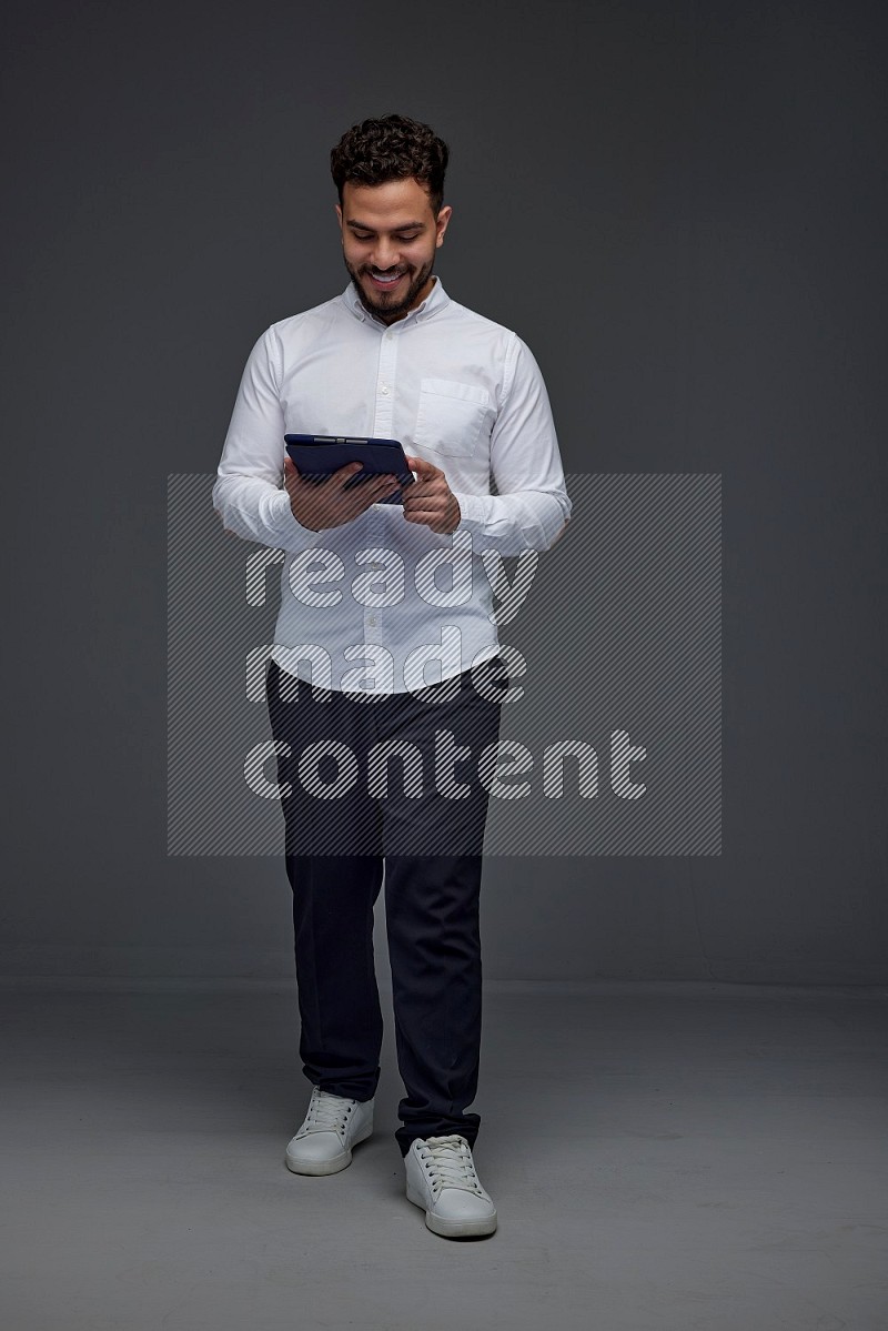 A man wearing smart casual standing and using his tablet eye level on a gray background