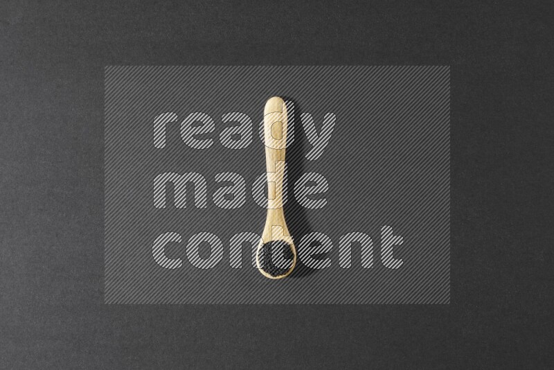 A wooden spoon full of black seeds on a black flooring