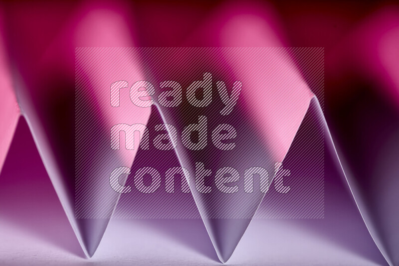A close-up abstract image showing sharp geometric paper folds in pink gradients