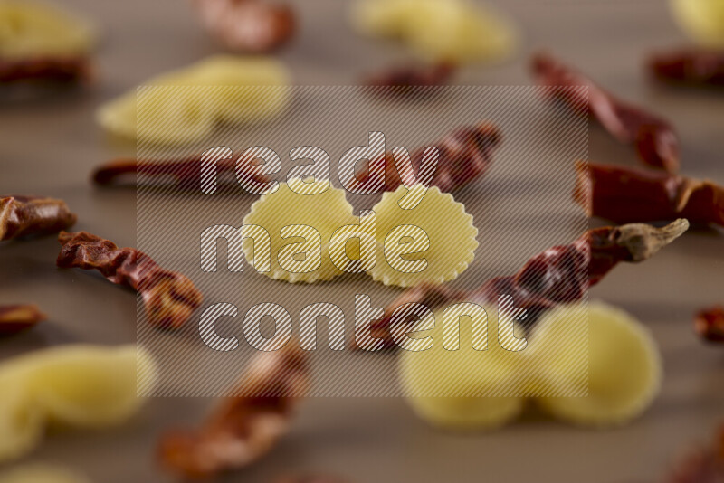 Raw pasta with different ingredients such as cherry tomatoes, garlic, onions, red chilis, black pepper, white pepper, bay laurel leaves, rosemary and cardamom on beige background