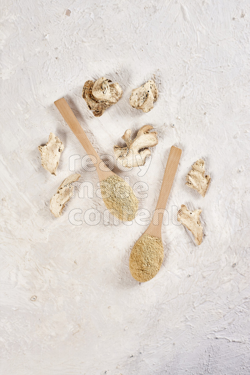 Two wooden spoons full of ground ginger powder on white background