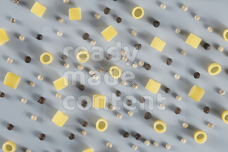 Raw pasta with different ingredients such as cherry tomatoes, garlic, onions, red chilis, black pepper, white pepper, bay laurel leaves, rosemary, cardamom and mushrooms on light blue background