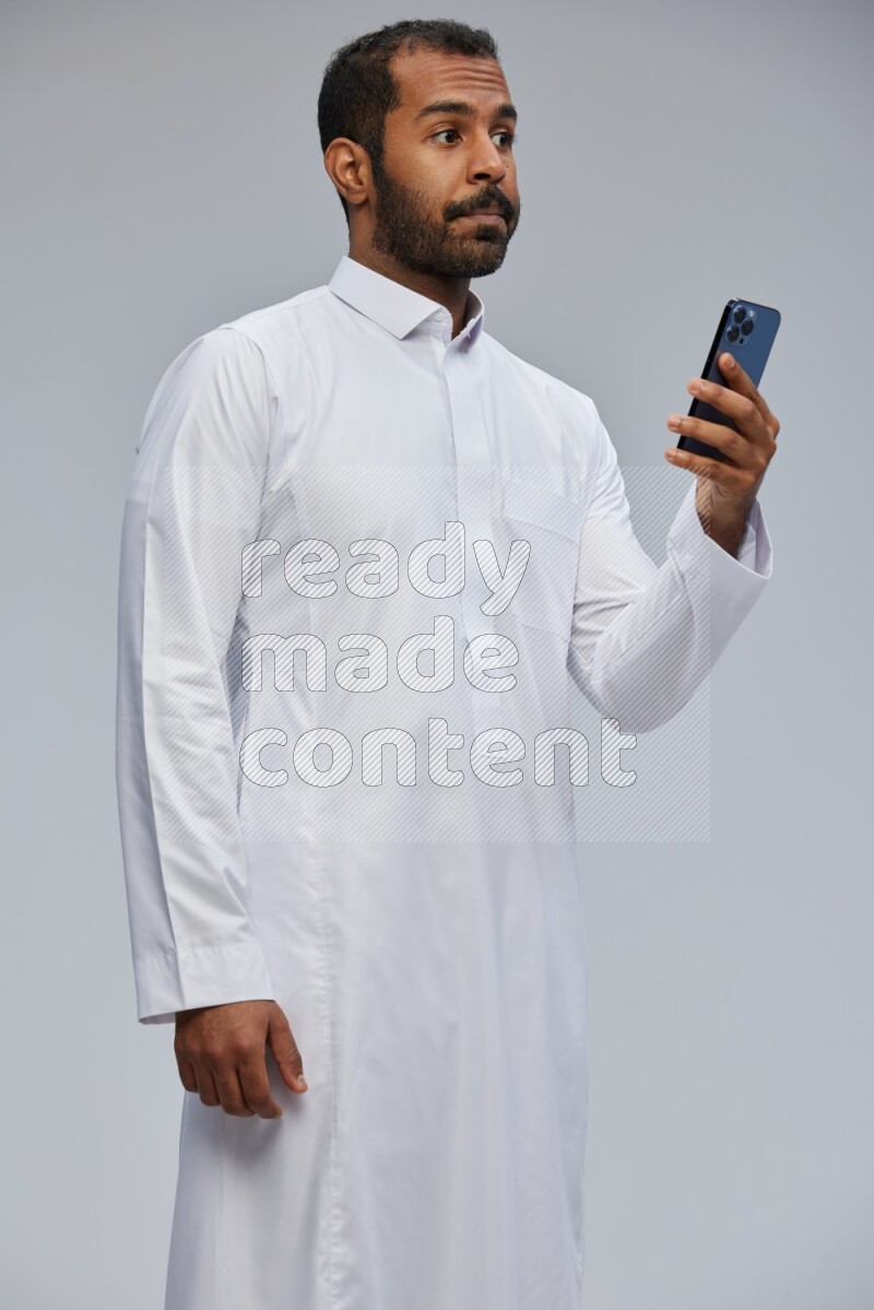 Saudi man wearing Thob standing texting on phone on Gray background