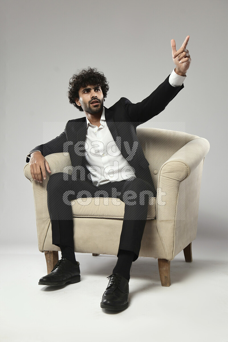 رجل يرتدي ملابس رسمية يجلس علي كرسي و يقوم بإشارات باليد علي خلفية بيضاء