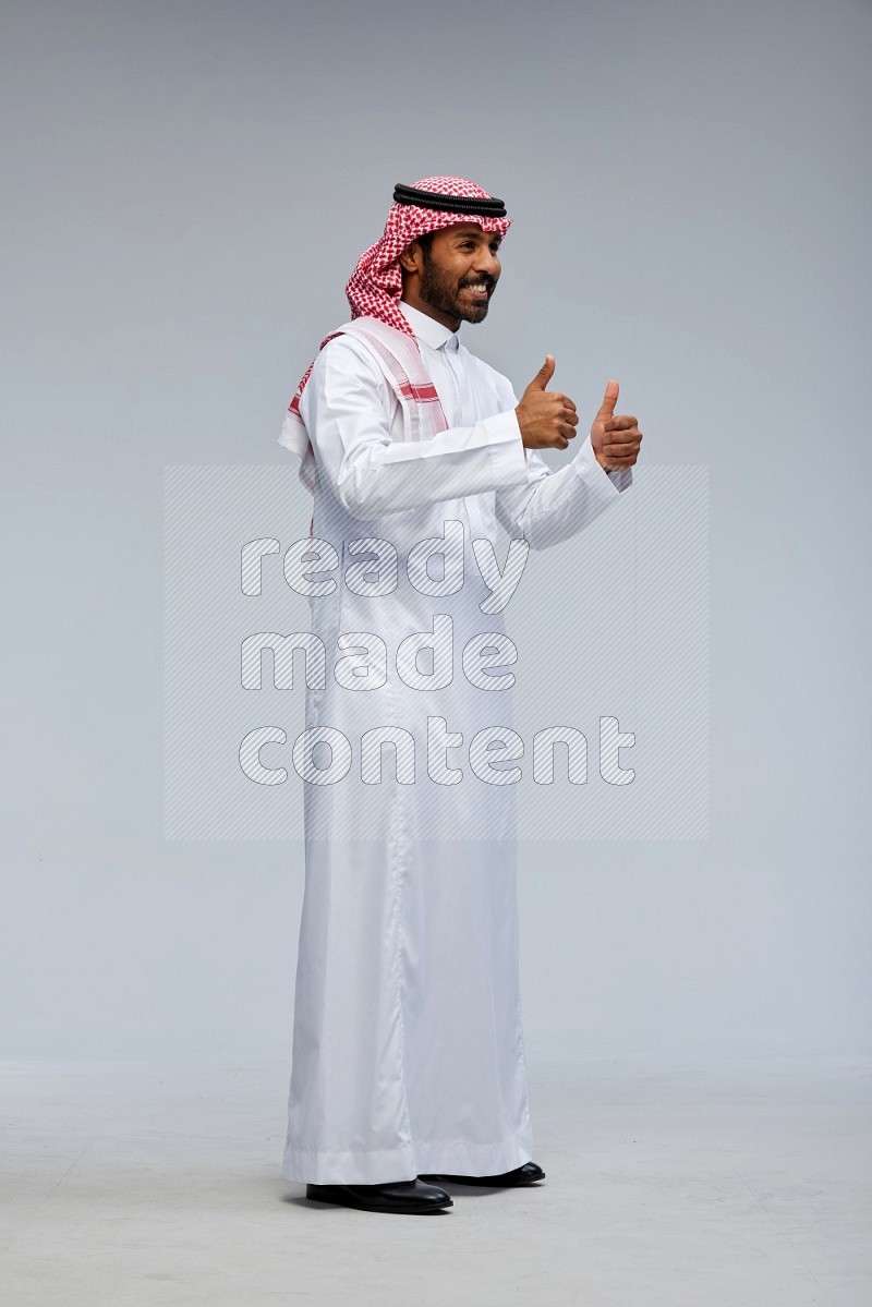 Saudi man Wearing Thob and shomag standing interacting with the camera on Gray background