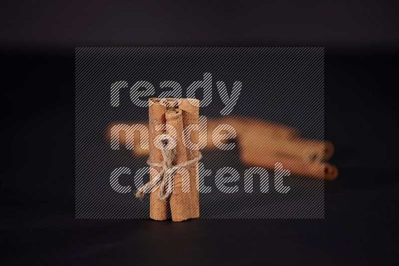 4 Cinnamon sticks stacked and bounded with more sticks in the background on black flooring