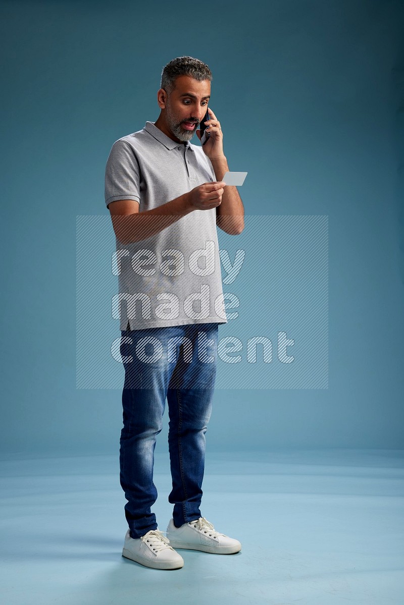 Man Standing holding ATM while talking on phone on blue background