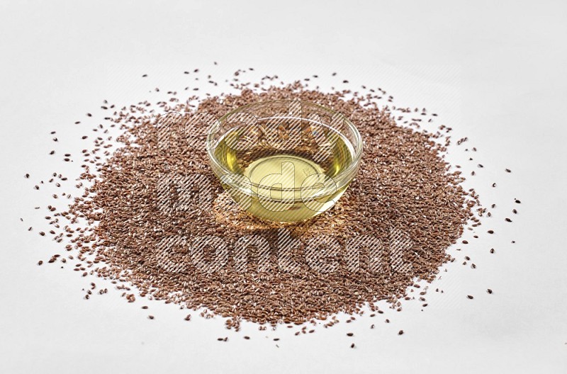 A glass jar full of flaxseeds oil surrounded by flax seeds on a white flooring