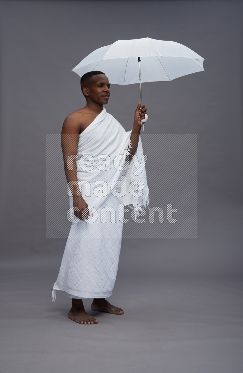 A man wearing Ehram Standing holding umbrella on gray background