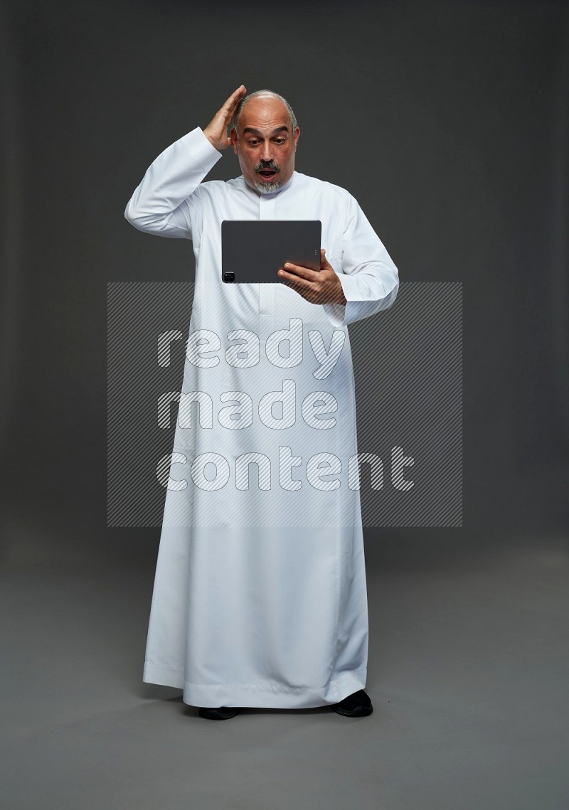 Saudi man without shomag Standing working on tablet on gray background