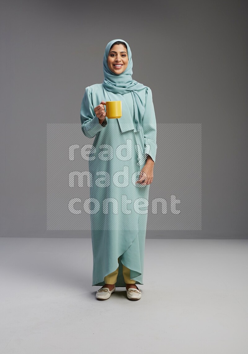 Saudi Woman wearing Abaya standing  holding a mug on Gray background