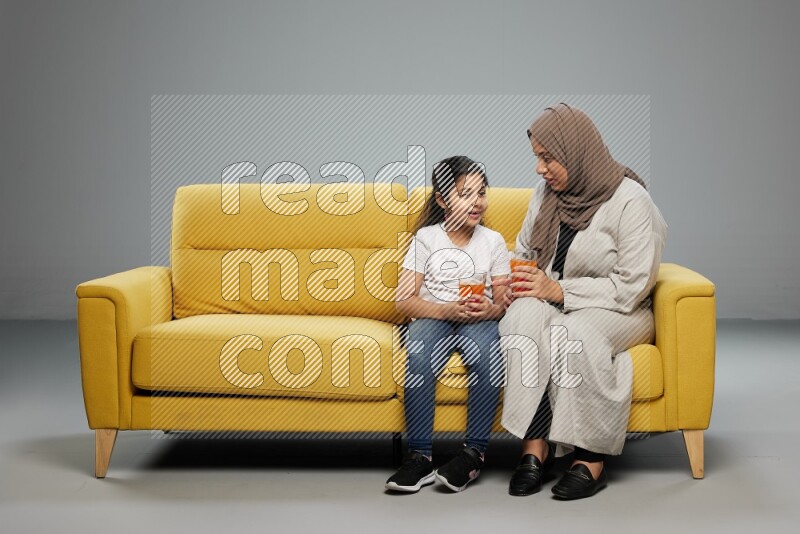 Mom and daughter sitting drinking juice on gray background