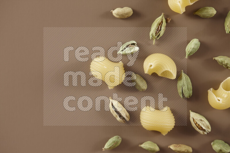 Raw pasta with different ingredients such as cherry tomatoes, garlic, onions, red chilis, black pepper, white pepper, bay laurel leaves, rosemary and cardamom on beige background