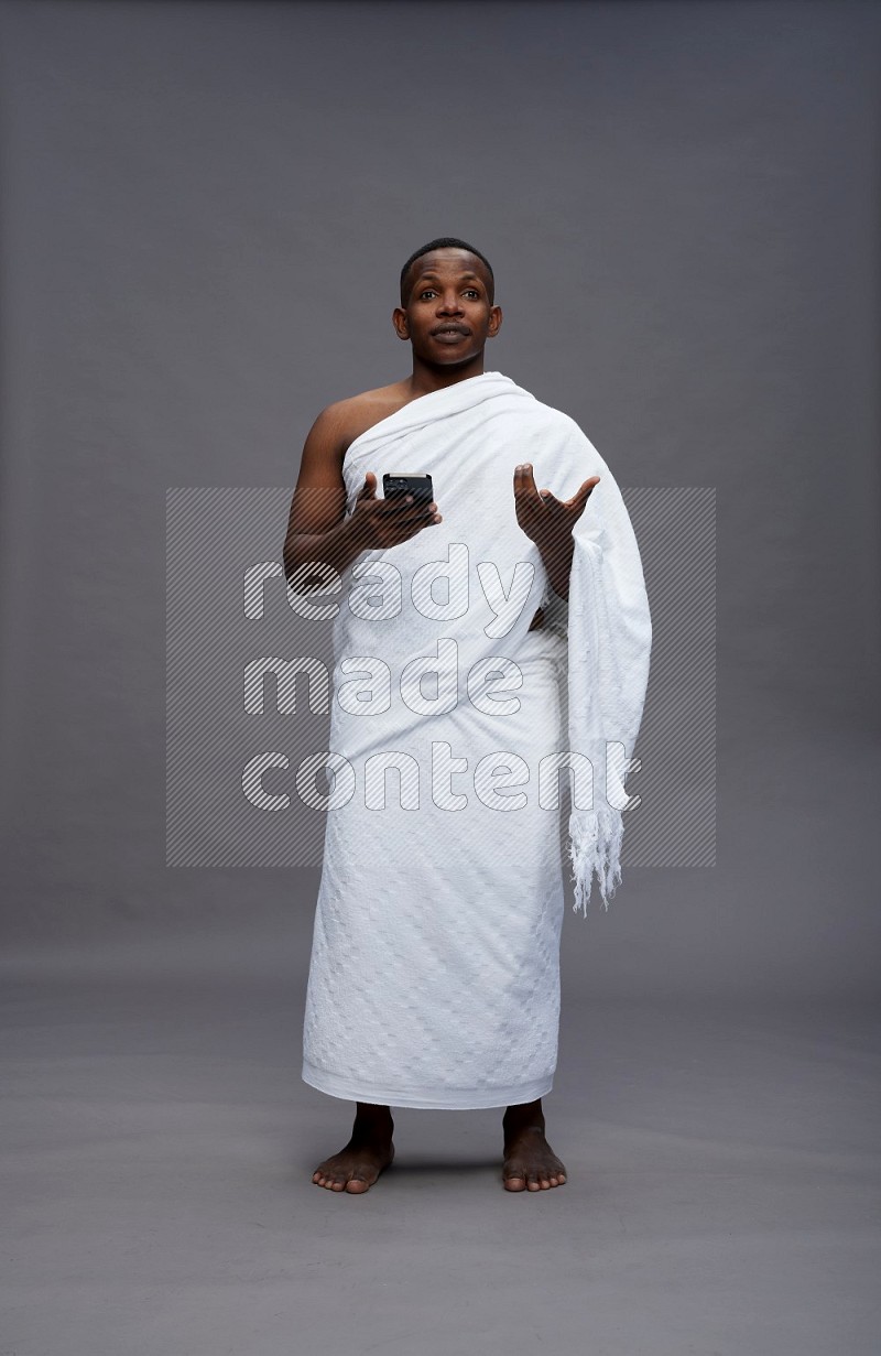 A man wearing Ehram Standing texting on phone on gray background