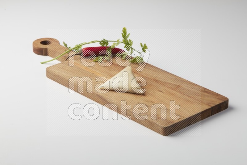 One uncooked samosa with a single red pepper and parsley on a wooden cutter on a white background