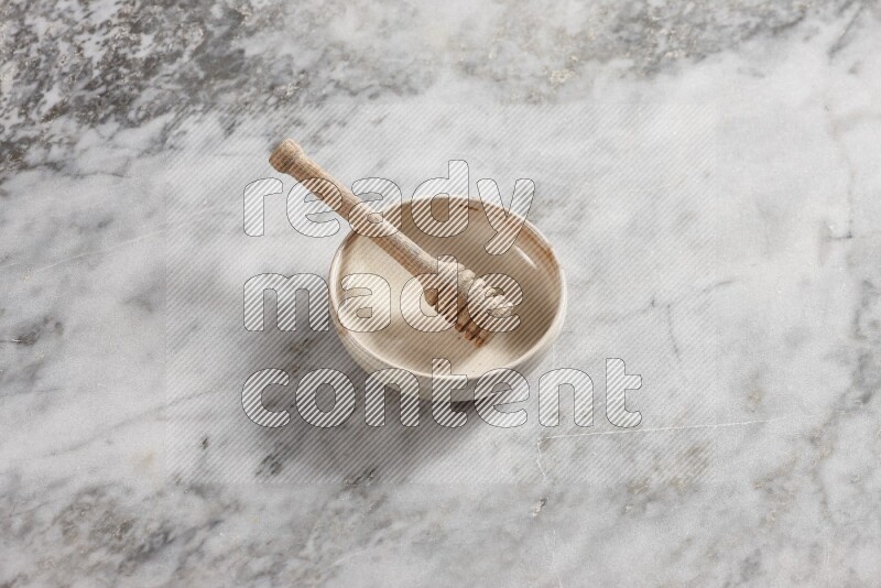 Beige pottery bowl with wooden honey dipper in it on grey marble background