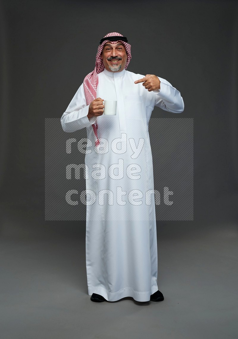 Saudi man with shomag Standing holding mug on gray background