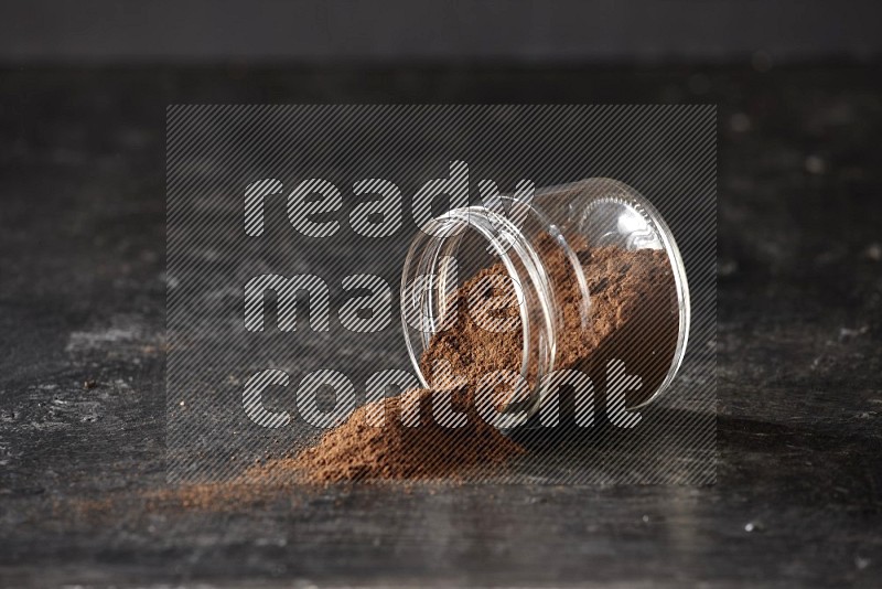 A flipped glass jar full of cloves powder on a textured black flooring