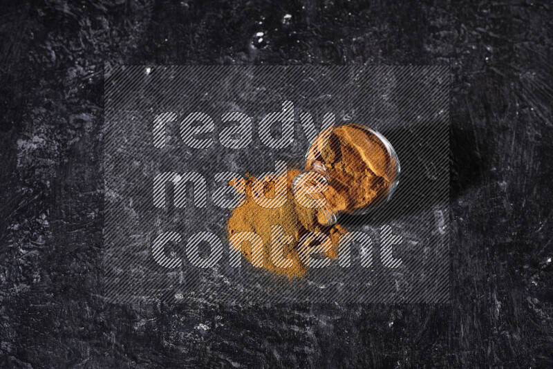 A glass jar full of ground paprika powder flipped with some spilling powder on black background