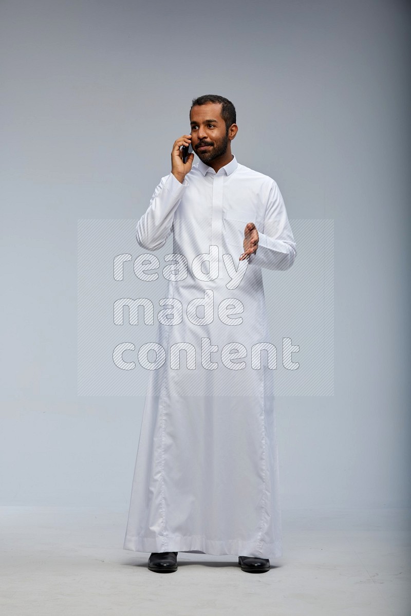 Saudi man wearing Thob standing talking on phone on Gray background